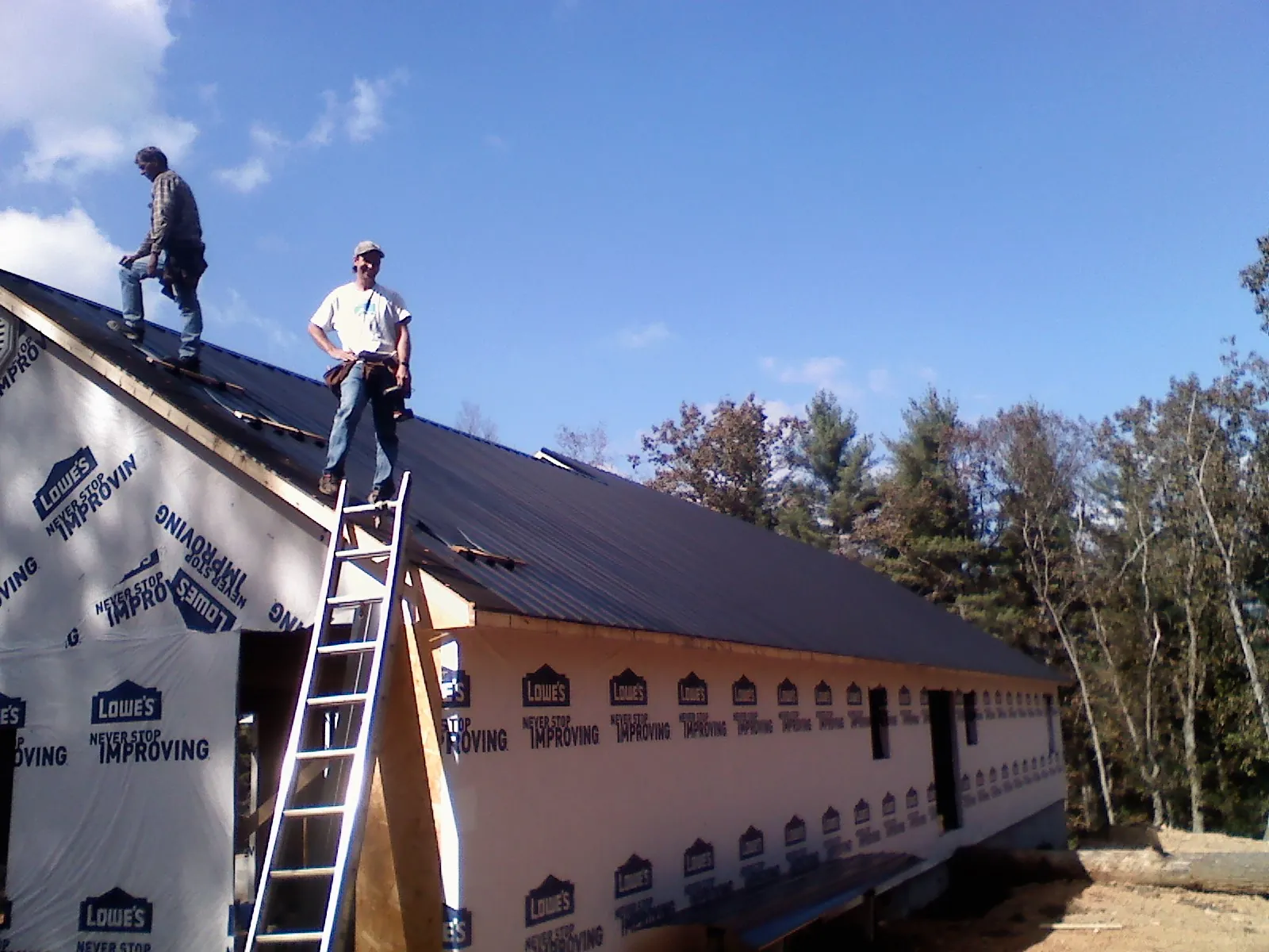 Two roofers standing on a long dark metal roof over a wrapped building in Oakland